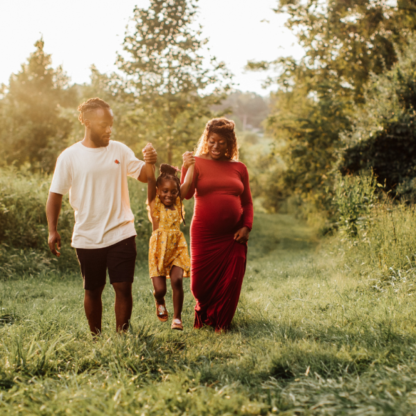 Husband and wife walking in the forest while swinging their child lightly by the arms.