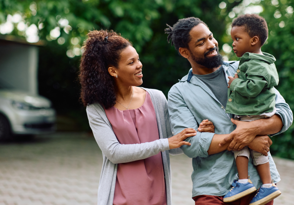 Happy family Husband and wife standing with their baby child. Husband is holding the child and the wife is holding the husbands arm. They just took out an insurance policy.
